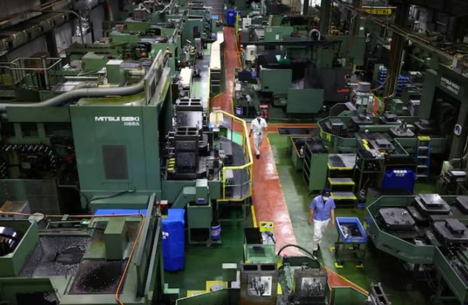 عمال يسيرون بين آلات دقيقة لتصنيع قطع غيار السيارات داخل مصنع شركة «كيوا» الصناعية في تاكاساكي (رويترز)