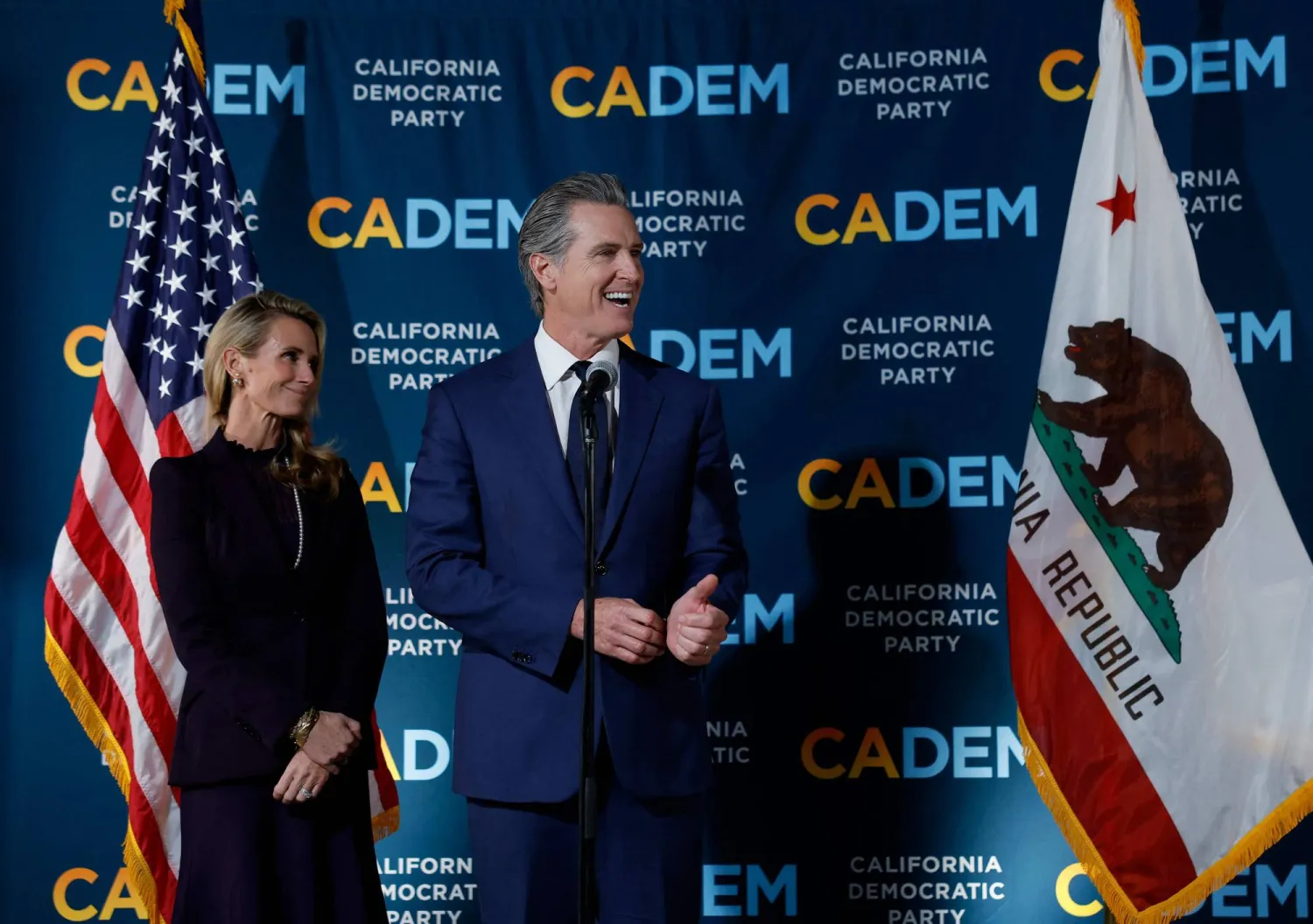 حاكم كاليفورنيا غافين نيوسوم (يمين) يتحدث بينما زوجته جينيفر سيبل نيوسوم (يسار) تُتابعه خلال اجتماع ليلة الانتخابات بمقر الحزب الديمقراطي بكاليفورنيا (أ.ف.ب)