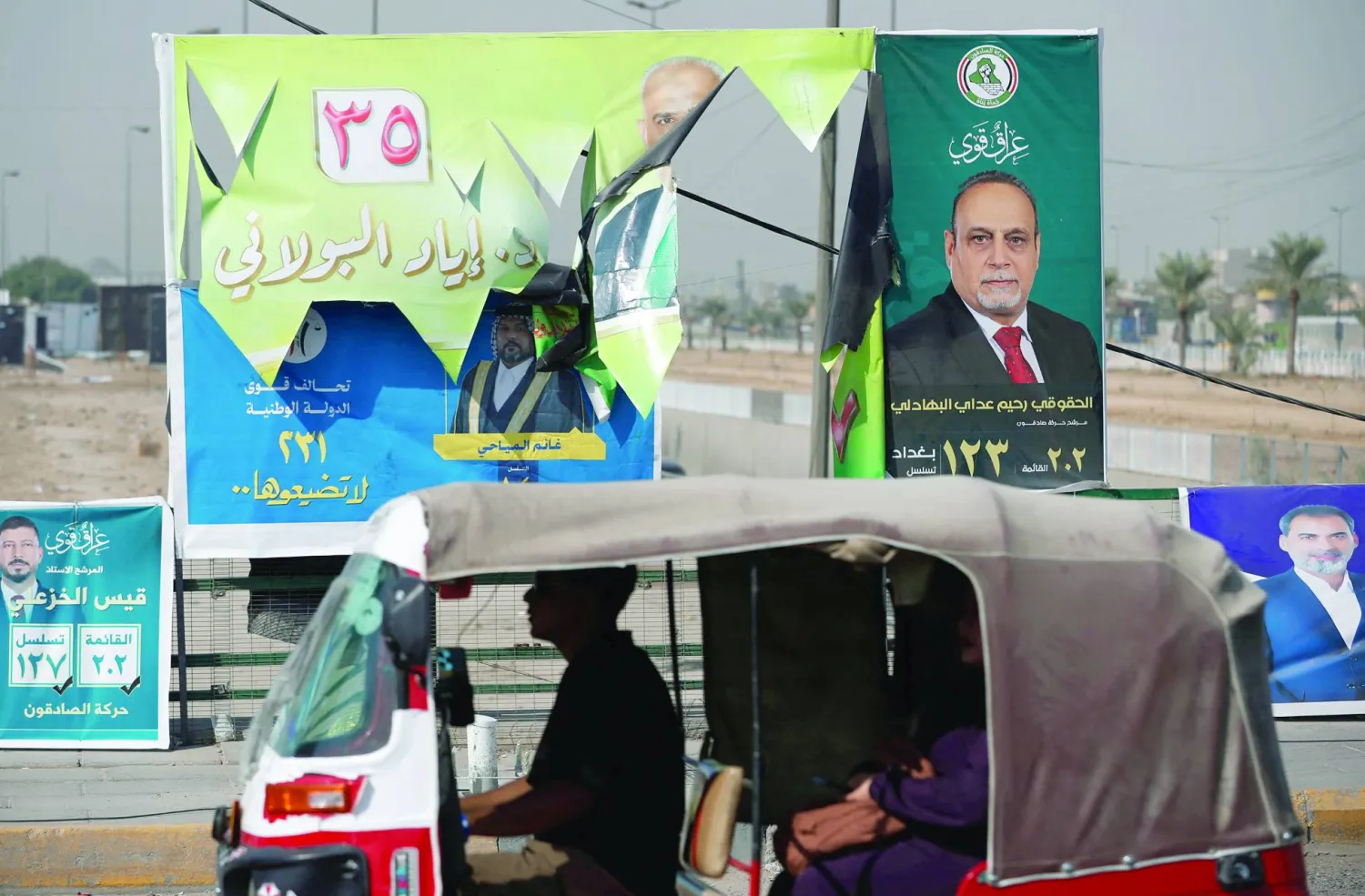 مركبة تمر أمام ملصقات انتخابية بمدينة الصدر شرق بغداد استعداداً للانتخابات البرلمانية (أ.ف.ب)