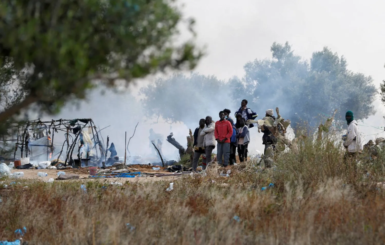 FILE PHOTO: Migrants gather near burnt tents, as Tunisian authorities have dismantled makeshift camps housing sub-Saharan African migrants, in Amra, Sfax, Tunisia April 24, 2025. REUTERS/Zoubeir Souissi/File Photo