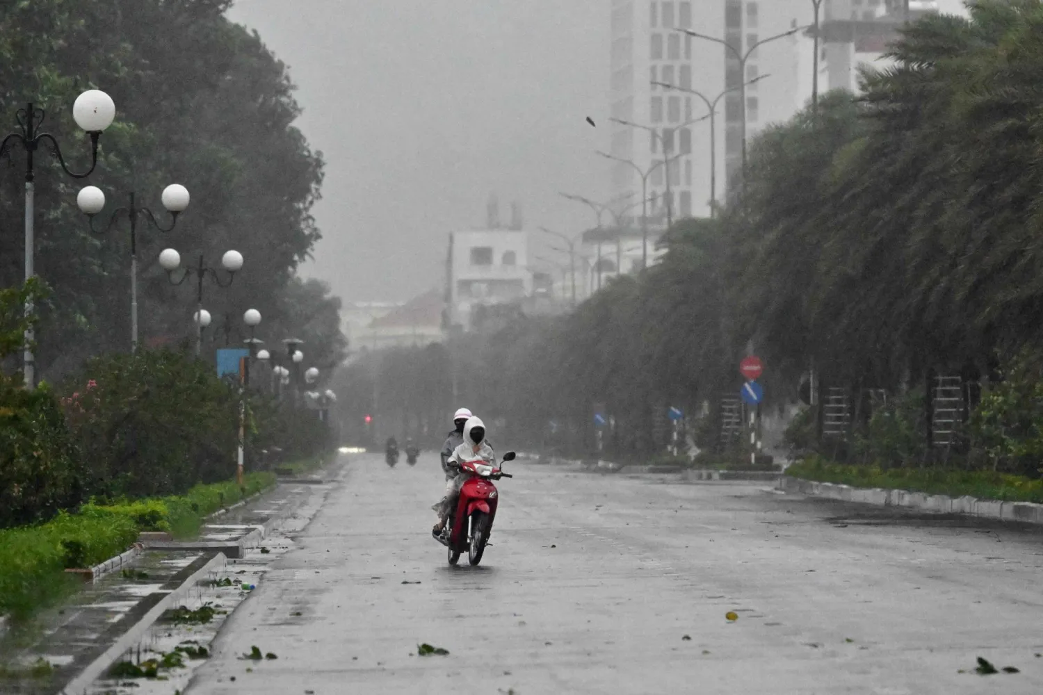 سائقون يركبون دراجة في ظل رياح قوية قبل وصول الإعصار «كالمايغي» على طريق بالقرب من شاطئ كوي نون وسط فيتنام (أ.ف.ب)