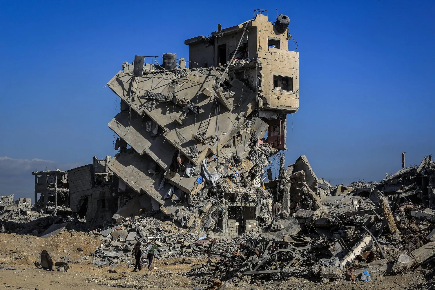 فلسطينيون يقفون أمام مبنى مدمر في خان يونس (د.ب.أ)