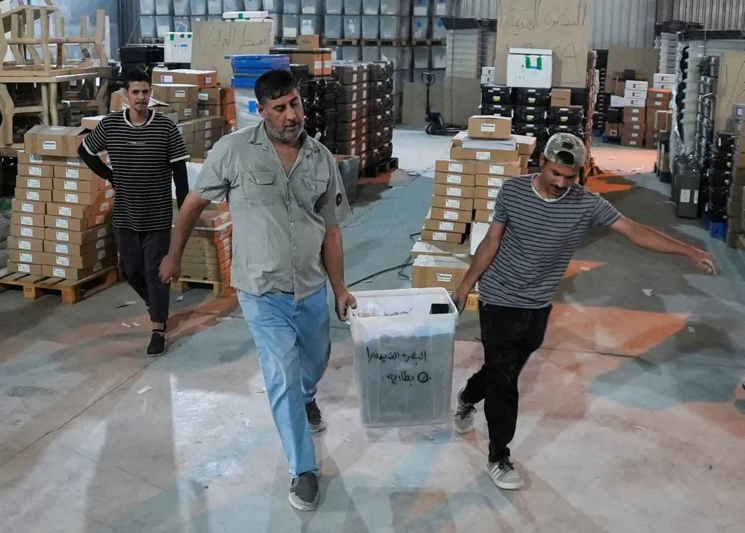 موظفون من مفوضية الانتخابات العراقية ينقلون صندوق اقتراع داخل مستودع في البصرة (رويترز)