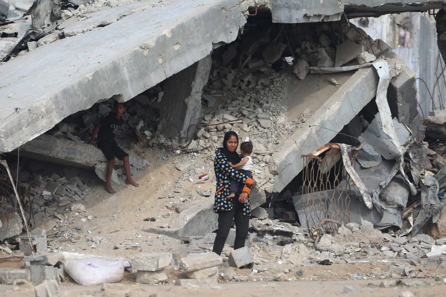 أم فلسطينية تحمل طفلها أمام مبان مدمرة على طريق قريب من مخيم النصيرات بوسط قطاع غزة يوم الأحد (أ.ف.ب)