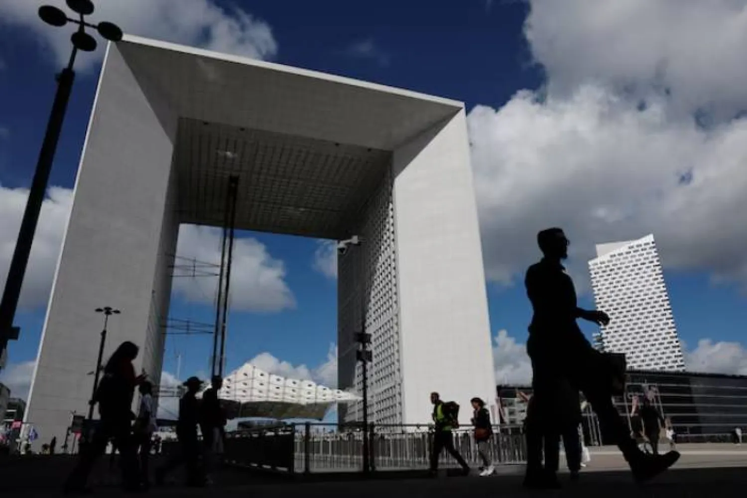 أشخاص يسيرون أمام القوس الكبير في حي لا ديفانس المالي والتجاري في بوتو بالقرب من باريس (رويترز)