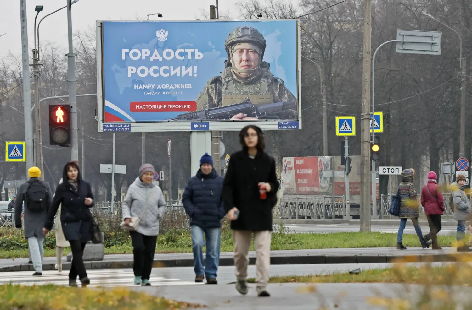 مواطنون روس يسيرون في أحد شوارع سان بطرسبورغ وخلفهم ملصق ضخم يصور جندياً مع كلام يقول: «فخر روسيا» (إ.ب.أ)