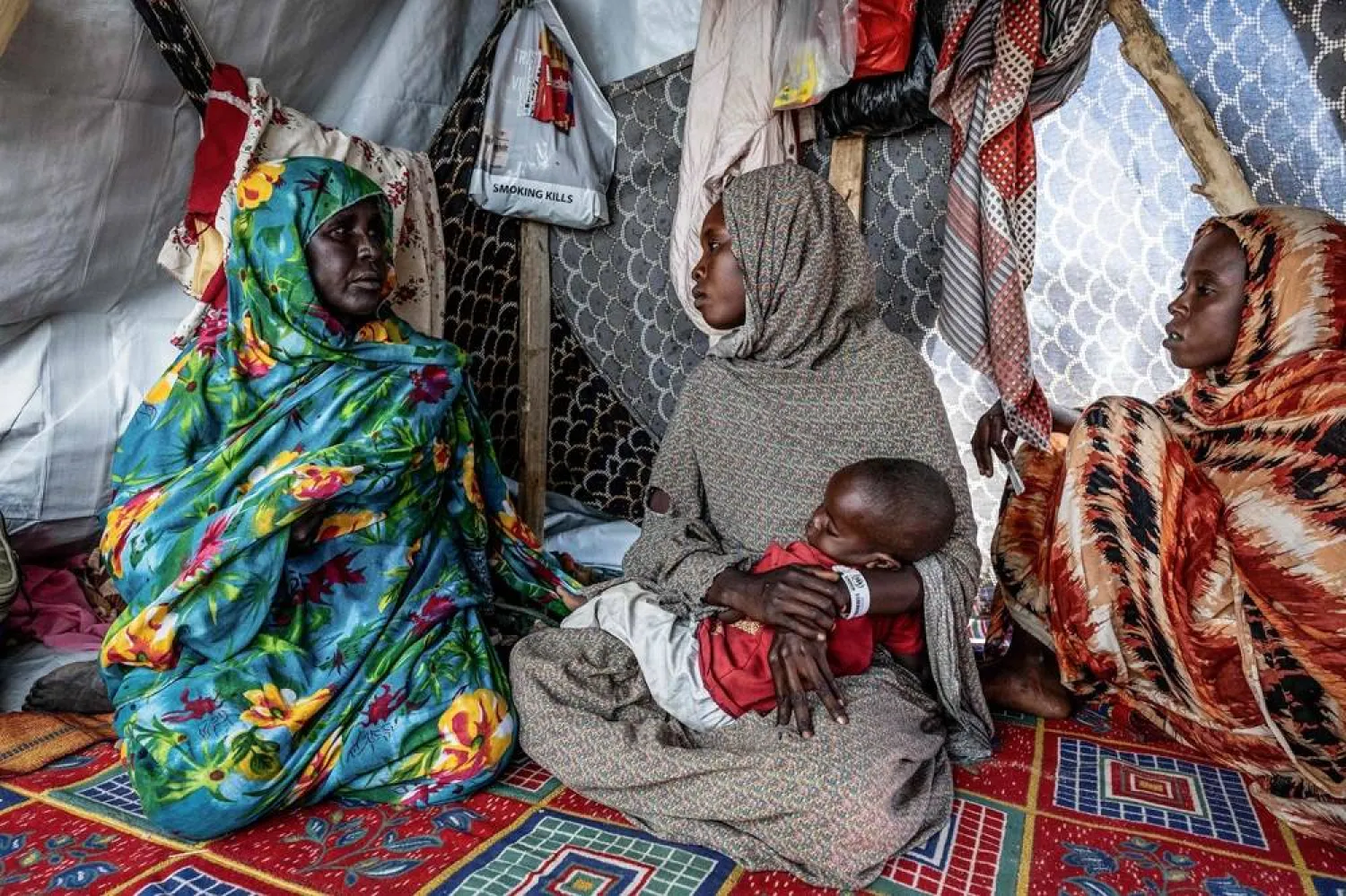 Sudanese refugee Mouda Youssouf Ahmat Fadoul, 23, (C) holds her baby while sitting inside a tent at the Tine transit camp in Chad on November 8, 2025. (AFP) 