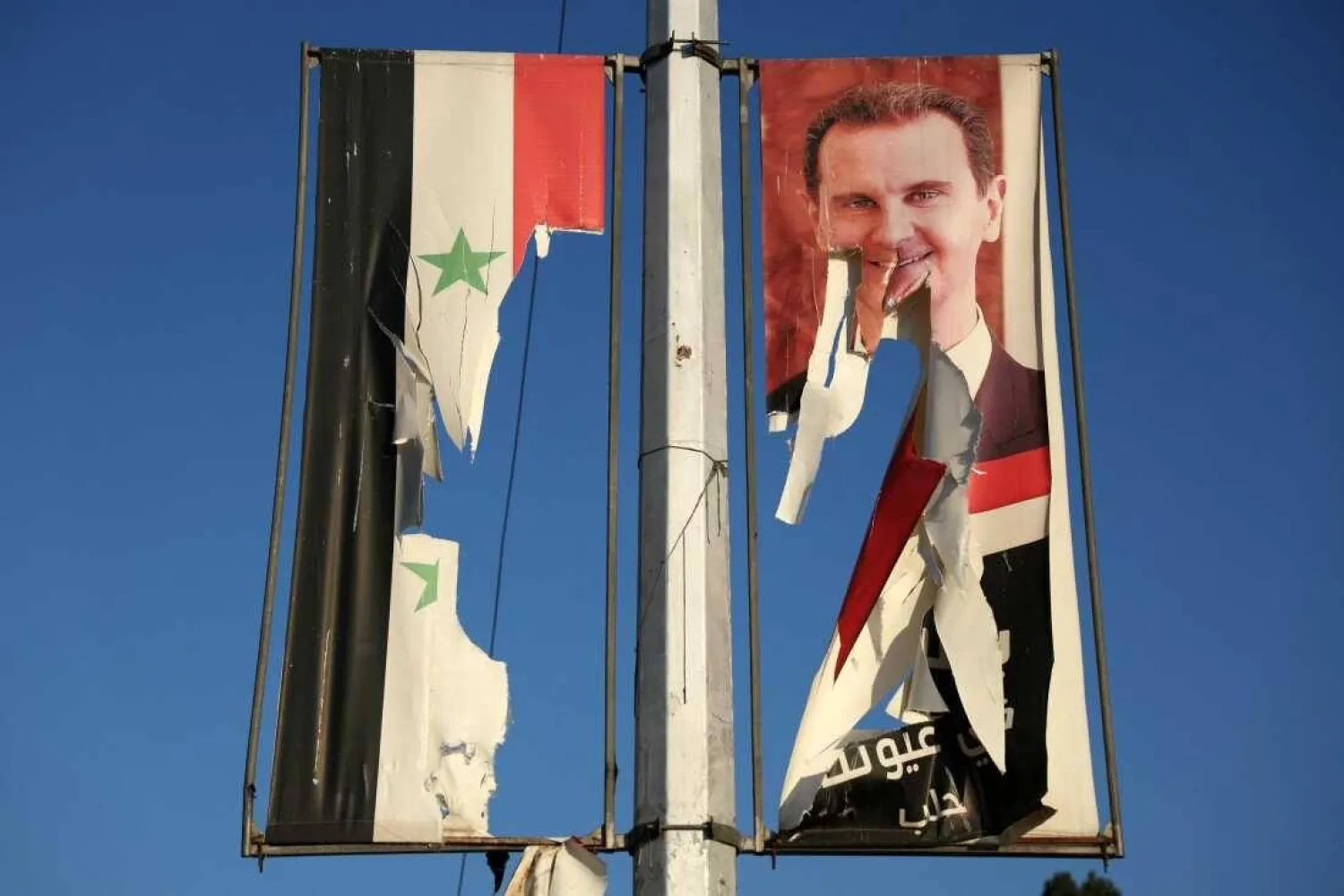 A billboard bearing a picture of Syria's ousted President Bashar al-Assad and a former national flag are torn by anti-government fighters in the northern city of Aleppo on Nov. 30. (AFP)