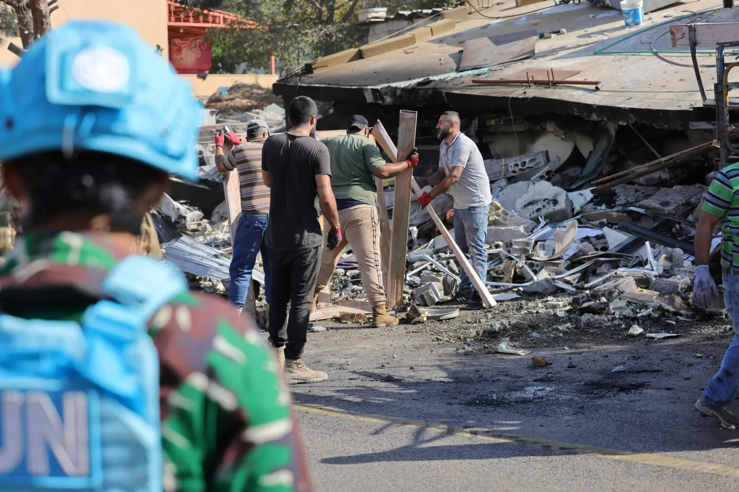 A UNIFIL member stands beside civilians clearing rubble from an Israeli airstrike that targeted Taybeh in southern Lebanon last Thursday (AFP). 