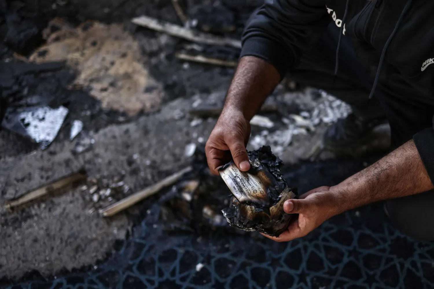 A Palestinian holds burnt Qur’an pages after a settler attack on Hajjah Hamidah mosque  in the village of Istiya, near Salfit, in the occupied West Bank (AFP)