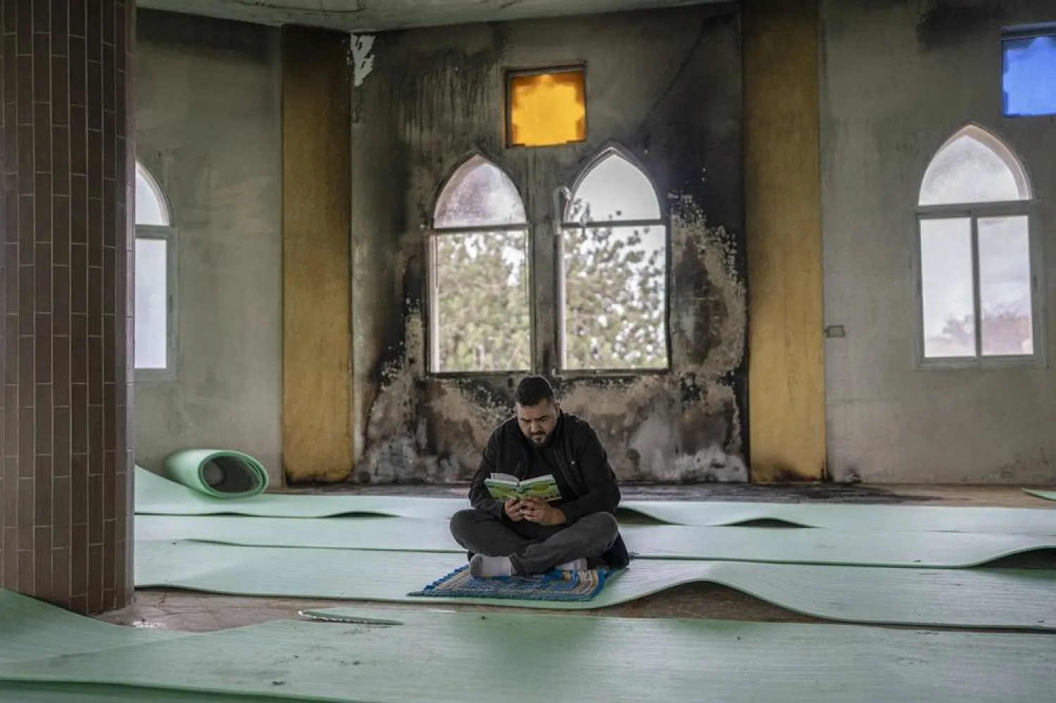  14 November 2025, Palestinian Territories, Salfit: A Palestinian man reads he holy Quran in front of a burned window before Friday prayer, inside the Hajjah Hamidah Mosque in the West Bank, one day after it was set on fire by Israeli settlers. (dpa)