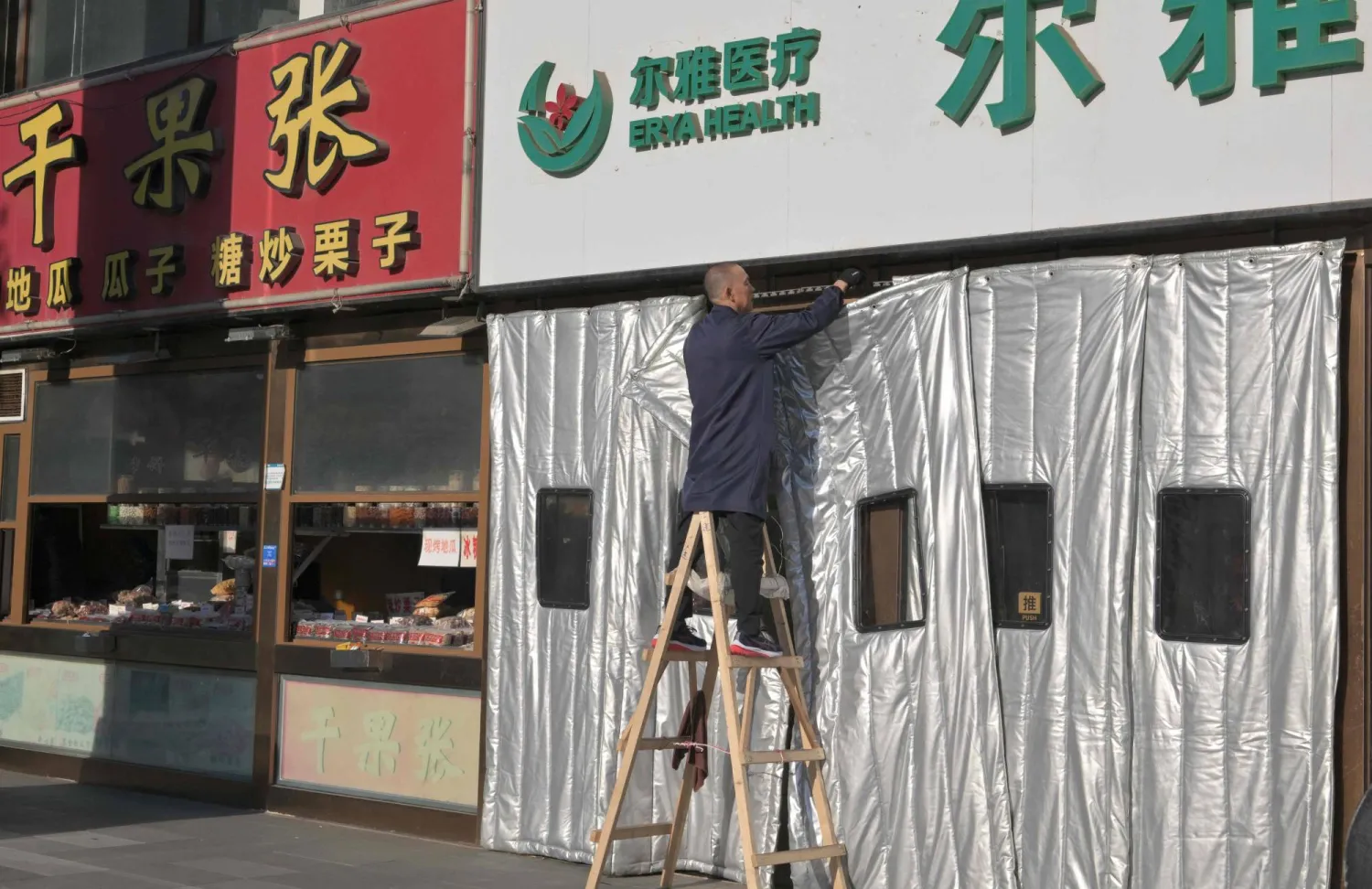 عامل يقوم بتركيب ستارة سميكة لفصل الشتاء في مجمع تجاري في بكين (أ.ف.ب)