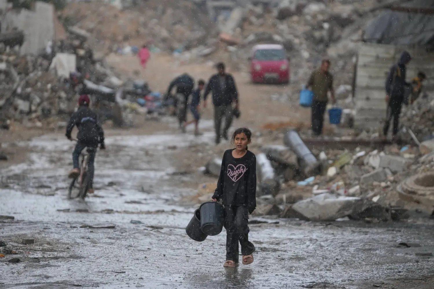 طفلة تحمل وعائين خاليين في طريقها لجلب المياه وسط أمطار غزيرة على حي الشيخ رضوان بمدينة غزة أمس (أ.ب)