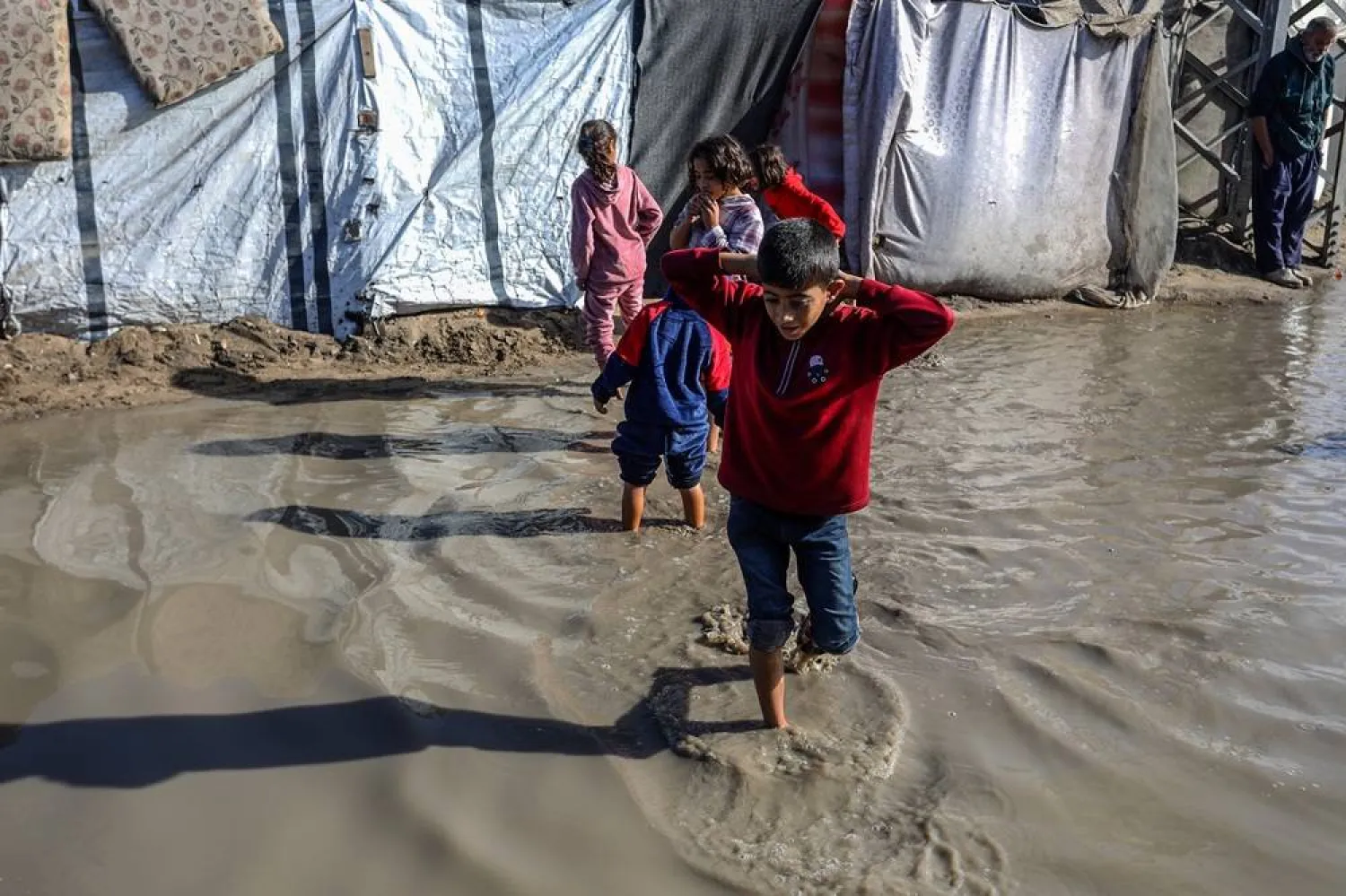 15 November 2025, Palestinian Territories, Khan Yunis: Children walk through the rainwater between their tents, as Palestinians suffer from the bitter cold and heavy rains that inundate their tents in the Al-Attar area of Mawasi, west of Khan Younis in the southern Gaza Strip. (dpa) 