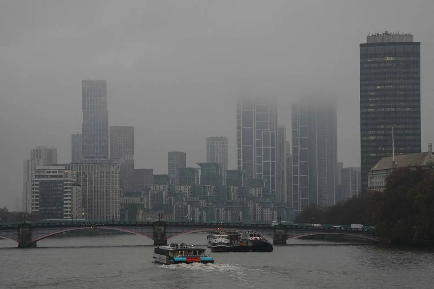  A catamaran (C) makes it way down the Thames towards high-rise buildings partly obscured by clouds in London on November 14, 2025, as inclement weather affects much of the country due to Storm Claudia. (AFP) 