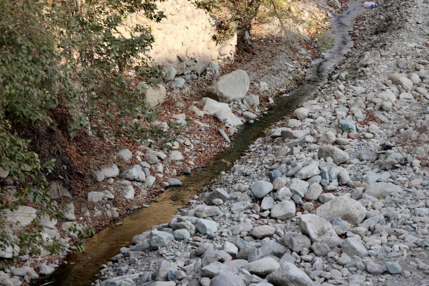 A trickle of water flows in the mainly dried-up Kan River, west of Tehran on November 9, 2025. (Photo by ATTA KENARE / AFP)