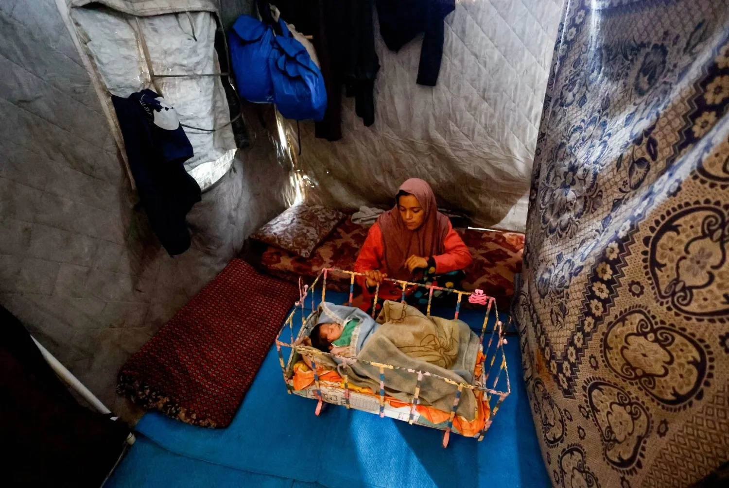 نازحة تنظر إلى طفلها داخل خيمة حاولت تحصينها من الأمطار بوسط قطاع غزة يوم الأحد (رويترز)