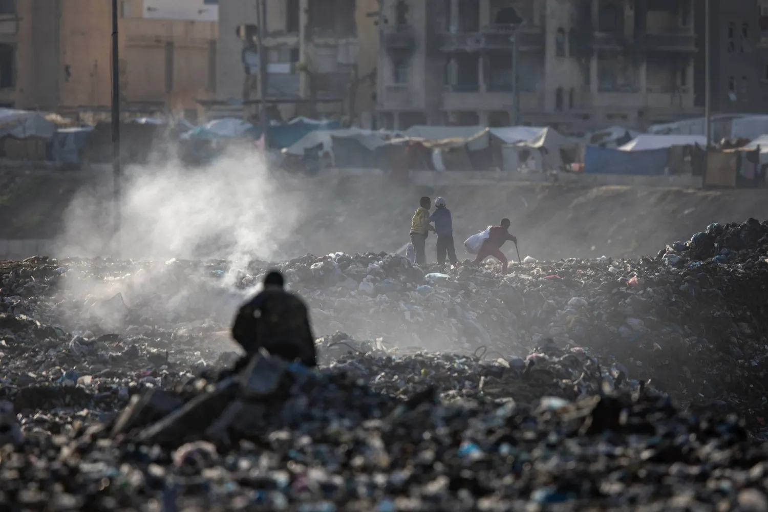 فلسطينيون يجمعون المخلفات البلاستيكية من بين أنقاض المباني في خان يونس بجنوب قطاع غزة (إ.ب.أ) 