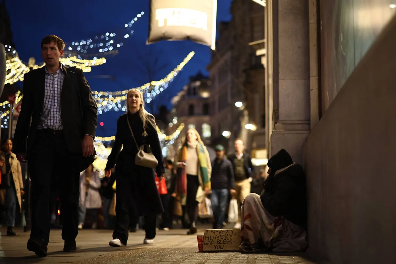 A beggar sits on the pavement on Regent Street as shoppers pass by on November 11, 2025 in London. (Photo by HENRY NICHOLLS / AFP)
