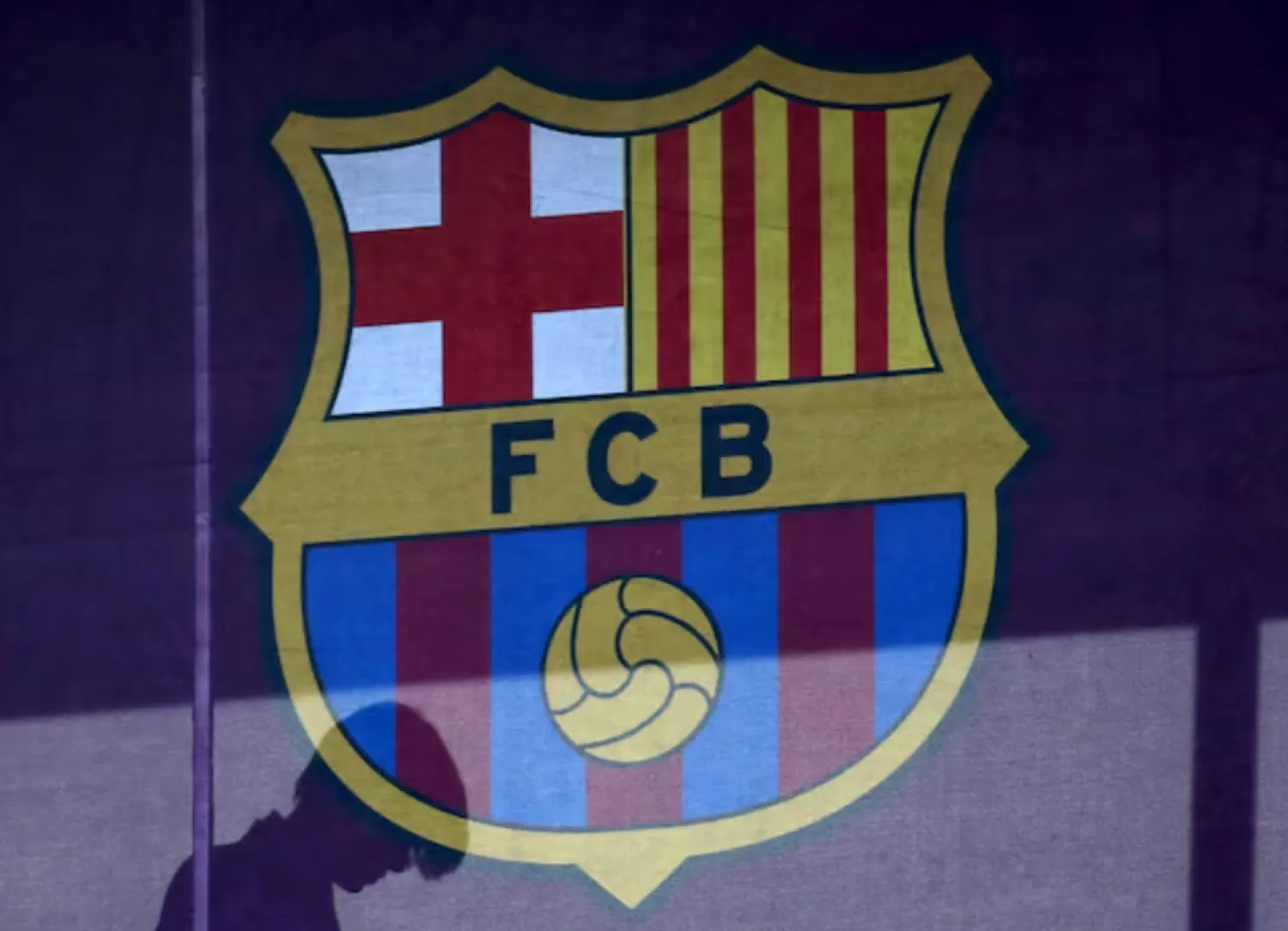 A silhouette of a woman walks past behind a FC Barcelona's logo at Camp Nou stadium in Barcelona, Spain, March 24, 2016. REUTERS/Albert Gea/File Photo 