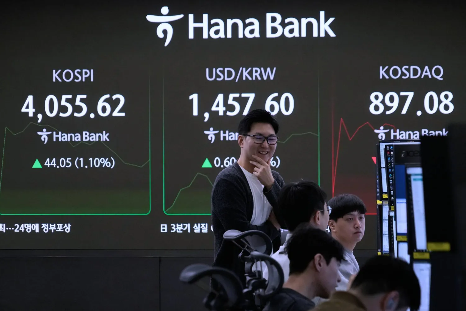 متداول يتحدث مع زملائه قرب شاشة تعرض مؤشر «كوسبي» وسعر صرف الدولار مقابل الوون في بنك هانا بسيول (أ ب)