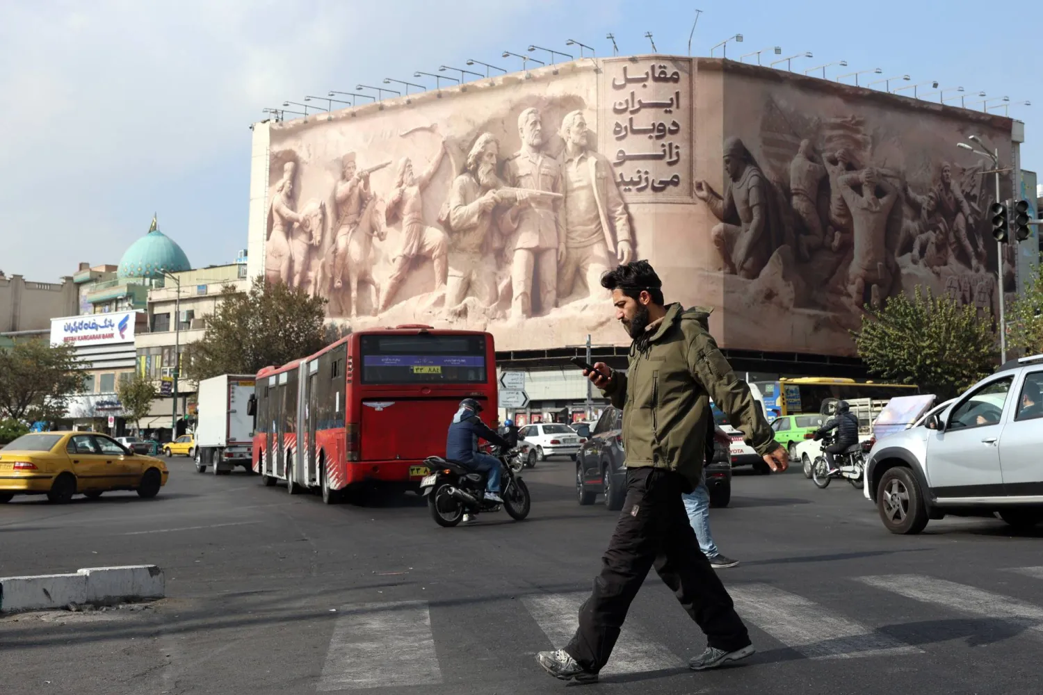 إيراني يعبر ميدان «انقلاب» وسط طهران بالقرب من لوحة إعلانية كُتب عليها بالفارسية: «ستركعون أمام إيران مرة أخرى» الاثنين (إ.ب.أ)