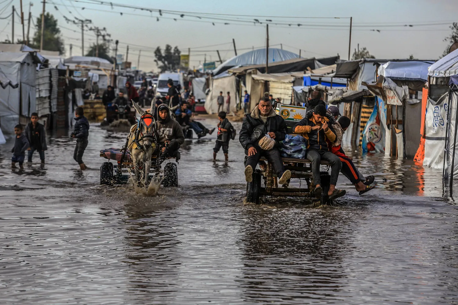 فلسطينيون يستخدمون عربات تجرها الحمير لعبور الشوارع الغارقة في ظل البرد القارس والأمطار الغزيرة بجنوب قطاع غزة (د.ب.أ)