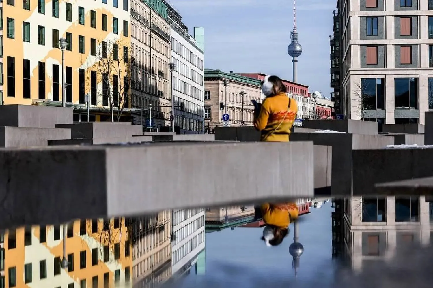 A reflection in a water puddle shows a pedestrian and Berlin TV Tower in central Berlin, Germany, 20 February 2025. (EPA)
