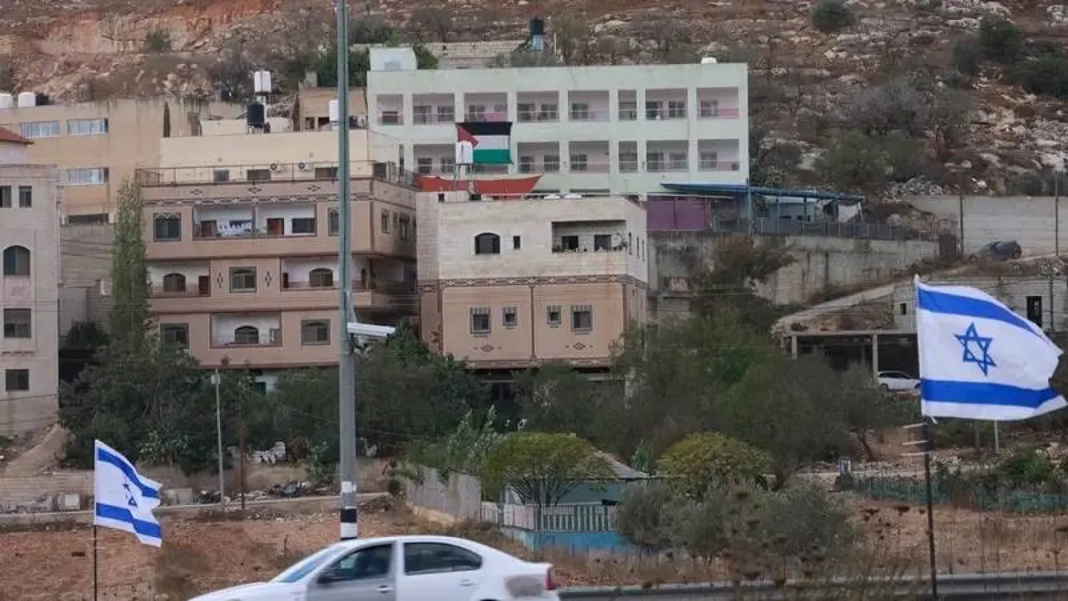 A Palestinian flag is seen on a building opposite Israeli national flags placed at the entrance of As-Sawiyah village, south of Nablus in the occupied West Bank, on November 16, 2025. (AFP)
