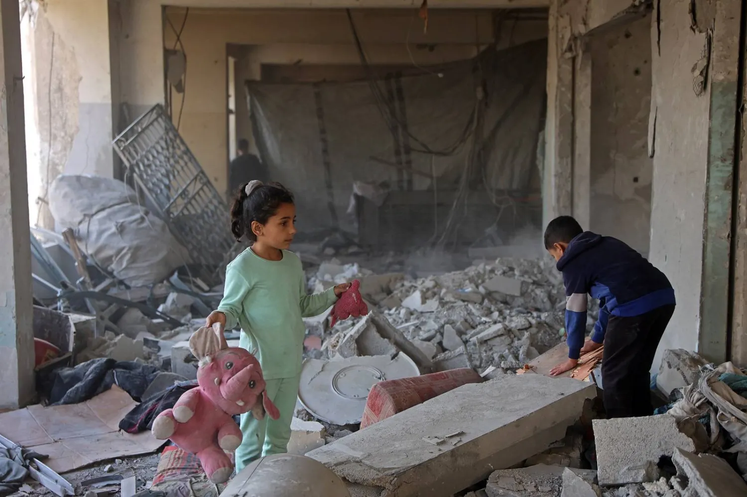 فتاة فلسطينية تحمل ألعابها وسط أنقاض مبنى مدمر تابع لوزارة الأوقاف كان يؤوي نازحين في حي الزيتون بمدينة غزة (أ.ف.ب)