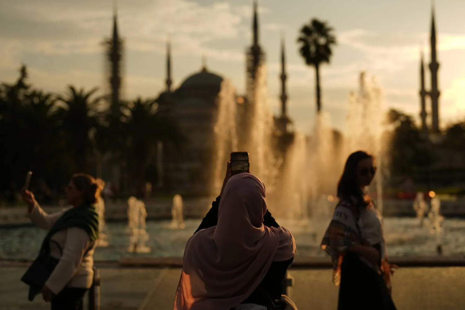 يلتقط الناس صوراً عند غروب الشمس خلف مسجد السلطان أحمد الذي يعود إلى العصر العثماني (أ.ب)
