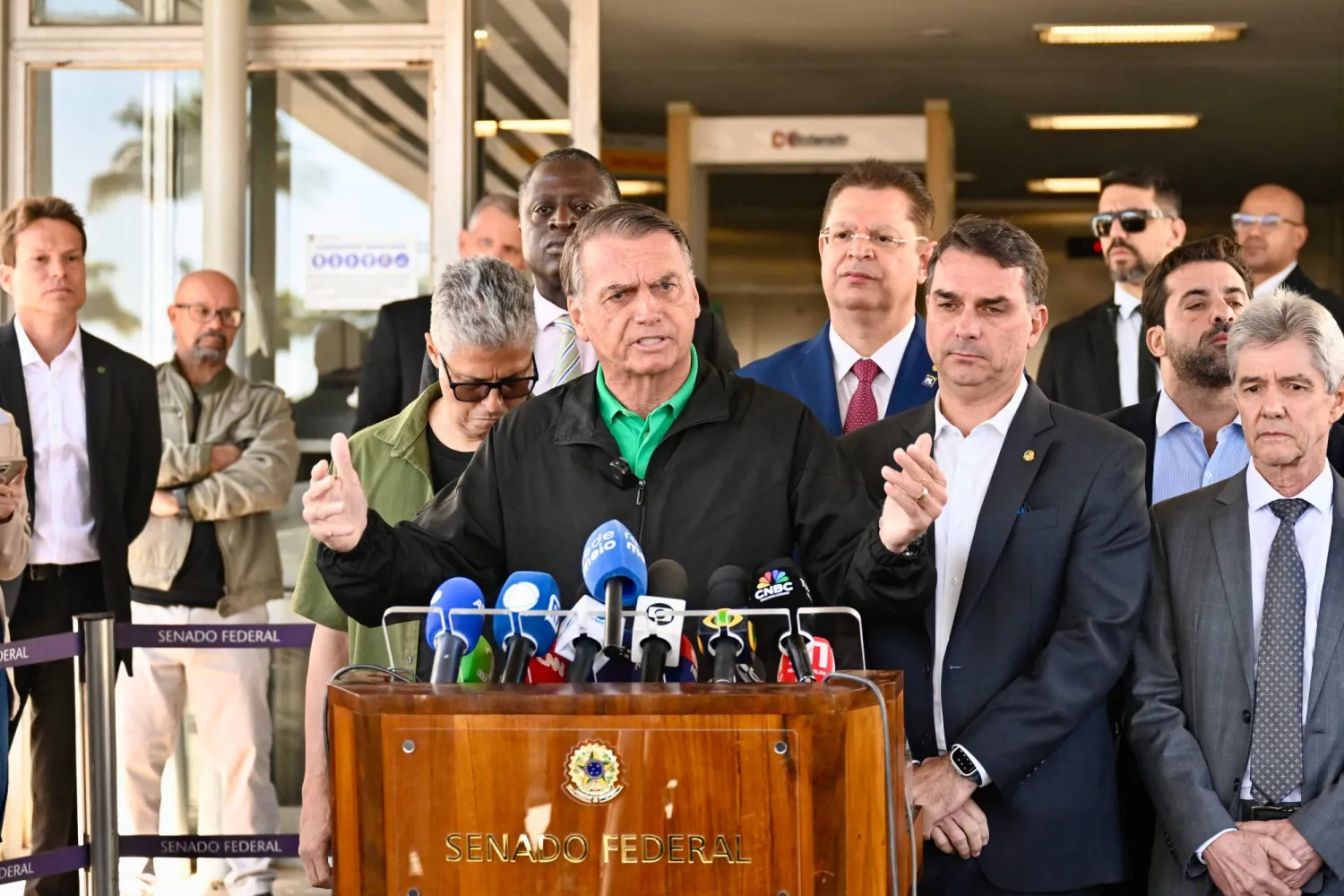 (FILES) Former Brazilian President Jair Bolsonaro speaks to the press next to his son Senator Flavio Bolsonaro at the Federal Senate in Brasilia on July 17, 2025. (Photo by Mateus Bonomi / AFP)