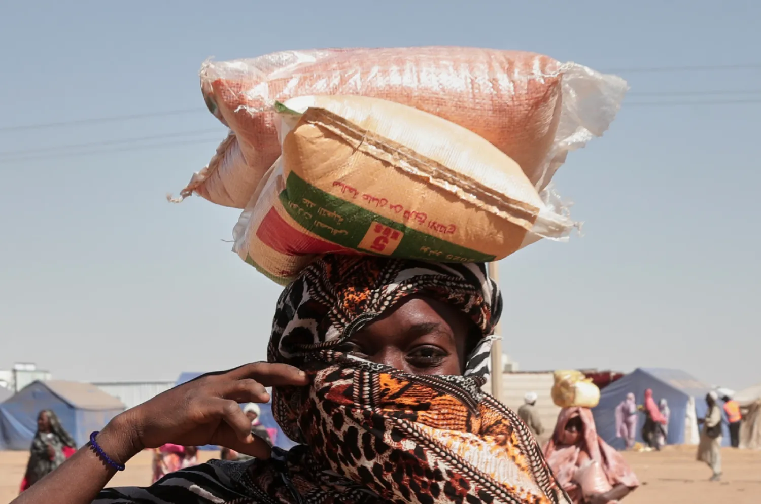 A Sudanese woman displaced from El-Fasher carries sacks of food aid on her head at the newly established El-Afadh camp in Al Dabbah, in Sudan's Northern State, Sunday, Nov. 16, 2025. (AP Photo/Marwan Ali)