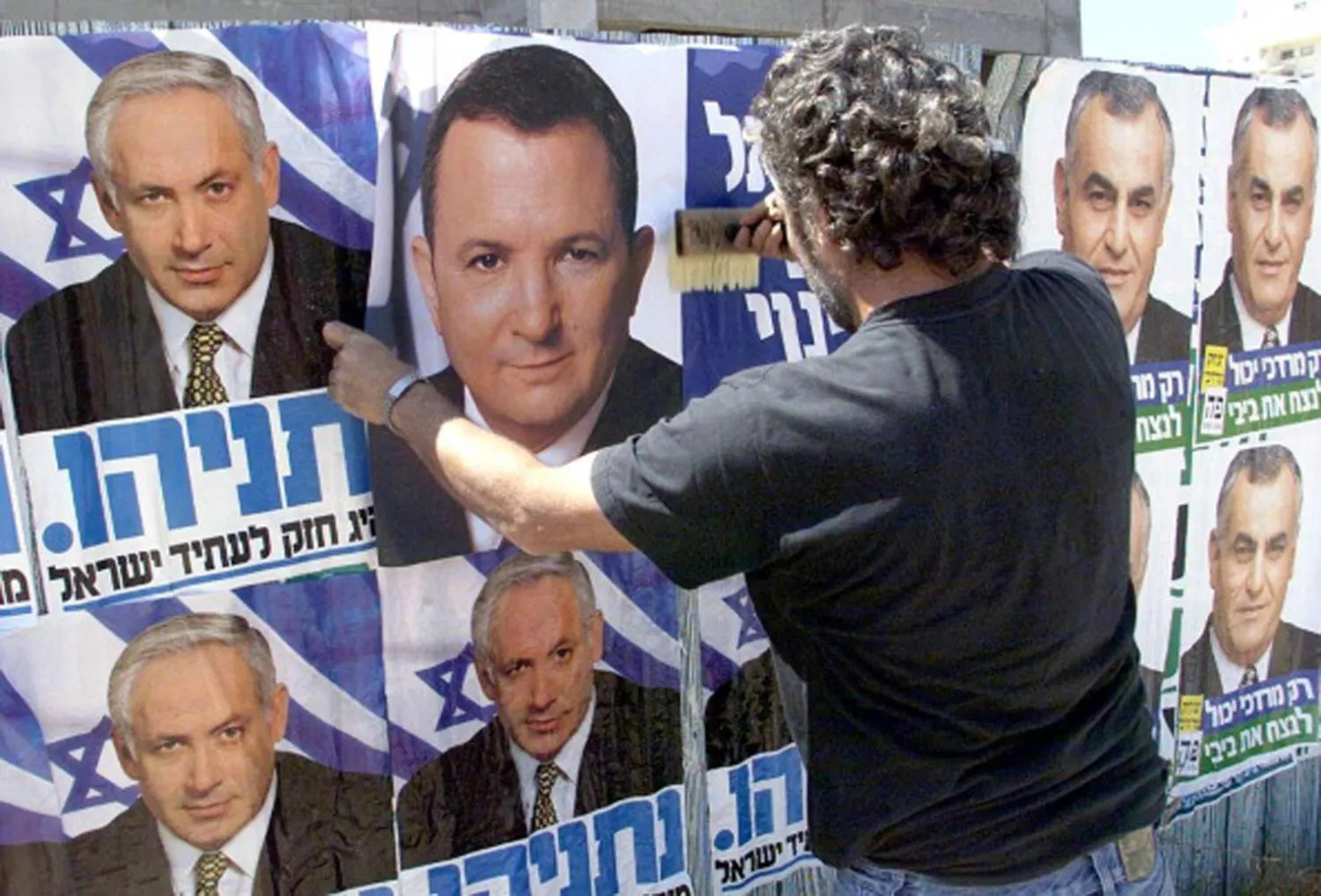 رجل يضع ملصقاً انتخابياً لإيهود باراك فوق صورة المرشح بنيامين نتنياهو في انتخابات 1999 (غيتي)