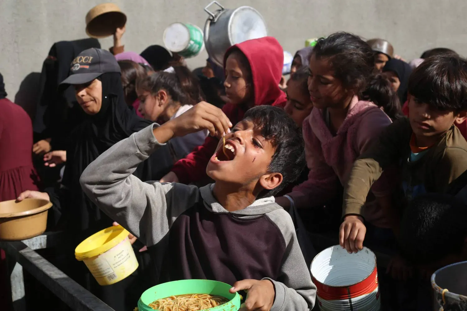 Gazze Şeridi'nin merkezindeki Nuseyrat'ta, ailelerin yaşadığı bir barınakta dün yiyecek aldıktan sonra yemek yiyen yerinden edilmiş bir Filistinli çocuk (AFP)
