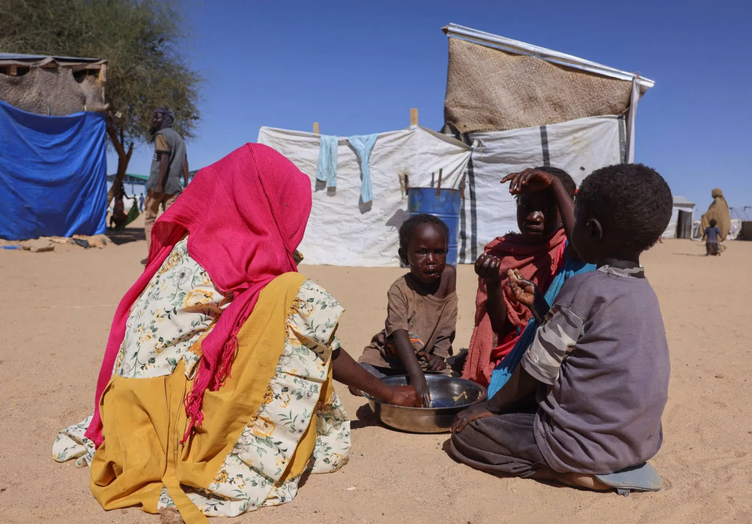 Sudanese refugee children from el-Fasher share a meal from a single plate at the Tine transit refugee camp, amid the conflict between the paramilitary Rapid Support Forces (RSF) and the Sudanese army, in eastern Chad, November 22, 2025. (Reuters)
