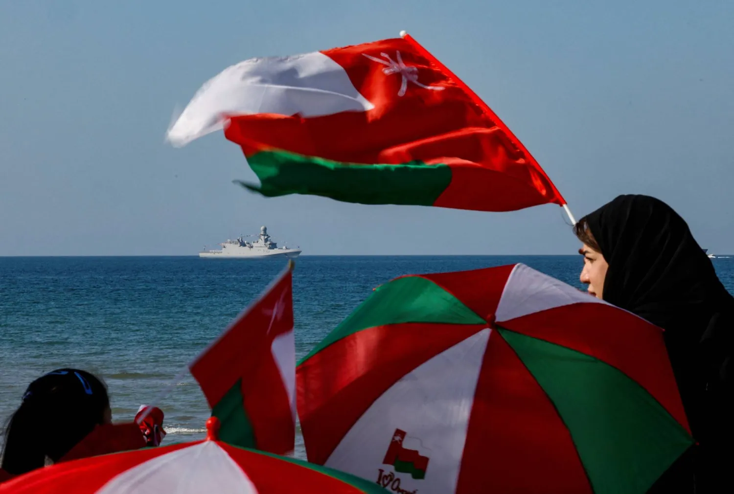 عمانية تلوّح بالعلم الوطني أثناء عرض عسكري للقوات البحرية خلال احتفالات اليوم الوطني على شاطئ القرم في مسقط (رويترز)