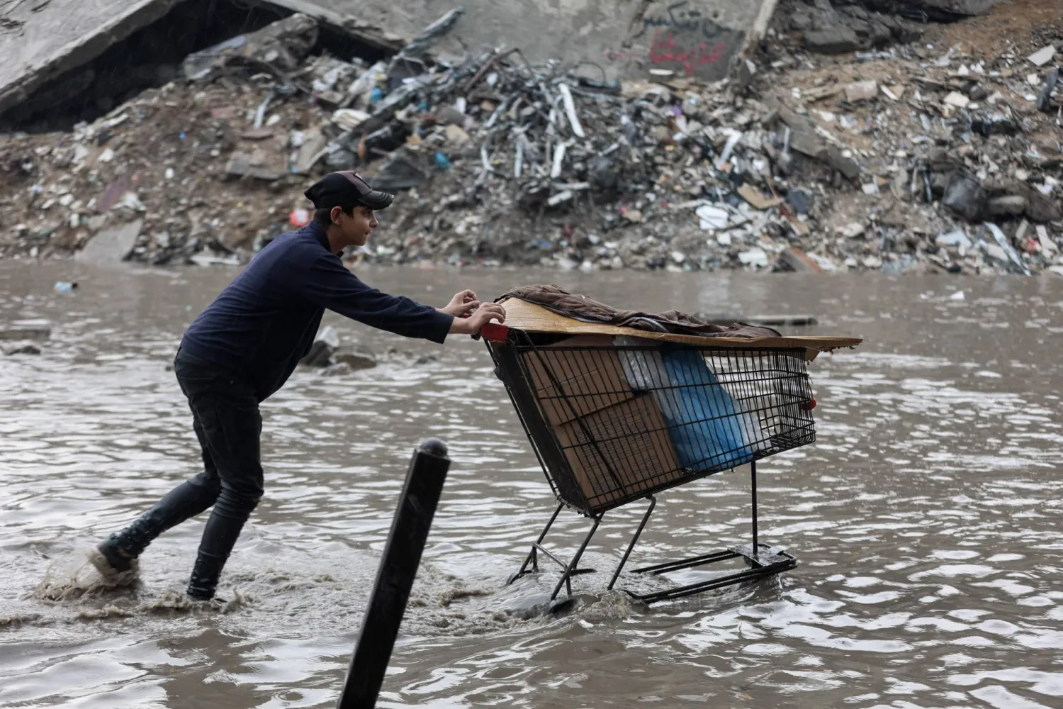 A man pushes a trolley in floodwaters at a makeshift camp housing displaced Palestinians following heavy rain in Gaza City on November 25, 2025. (AFP)