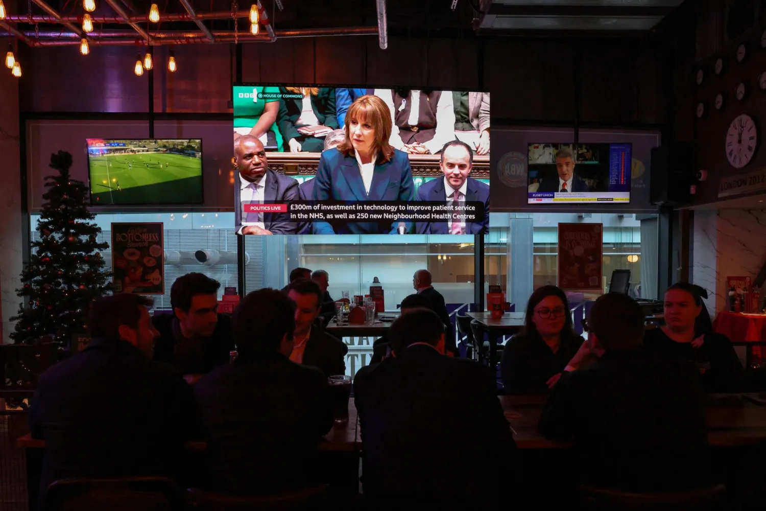 ريفز تظهر على شاشة تلفزيونية في مطعم في الحي المالي في كاناري وارف أثناء تقديمها بيان الموازنة في البرلمان (رويترز)