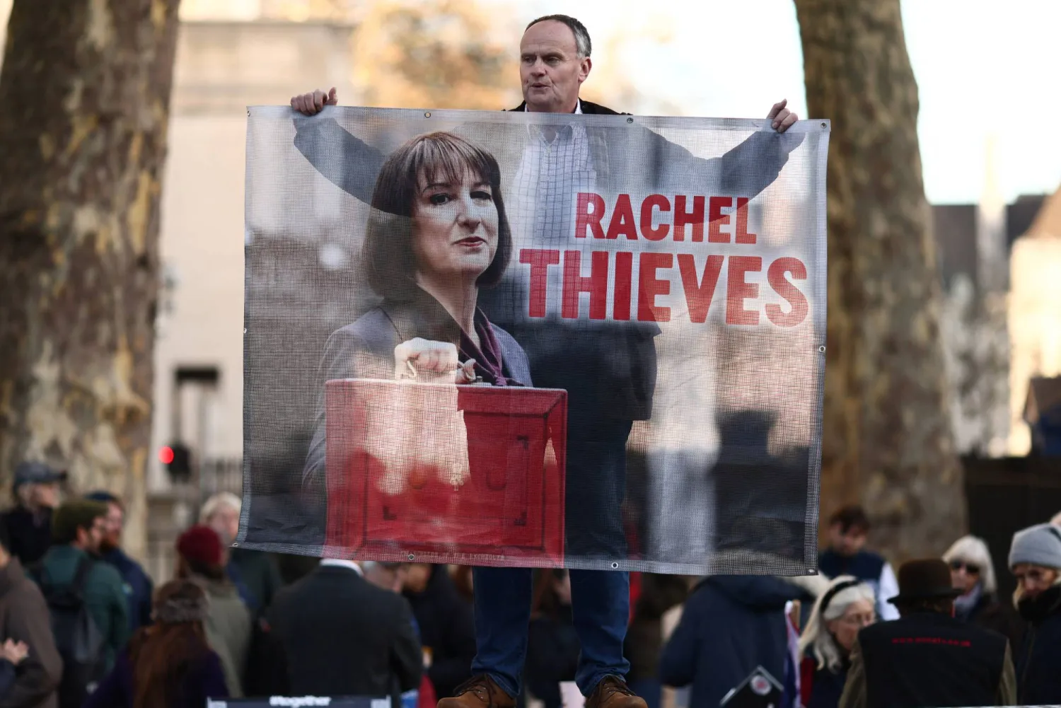 متظاهر يرفع لافتة كُتب عليها راشيل ثيفز مقابل داونينغ ستريت في اليوم الذي قدمت فيه ريفز بيان الموازنة (رويترز)