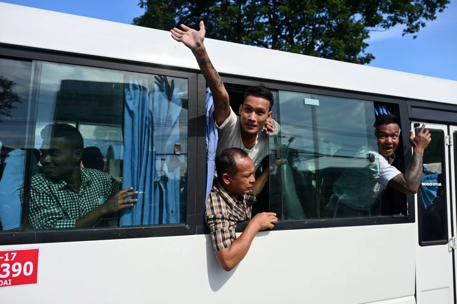 سجين مُفرج عنه يلوح بيده من حافلة خارج سجن إنسين في يانغون بميانمار (أ.ف.ب)