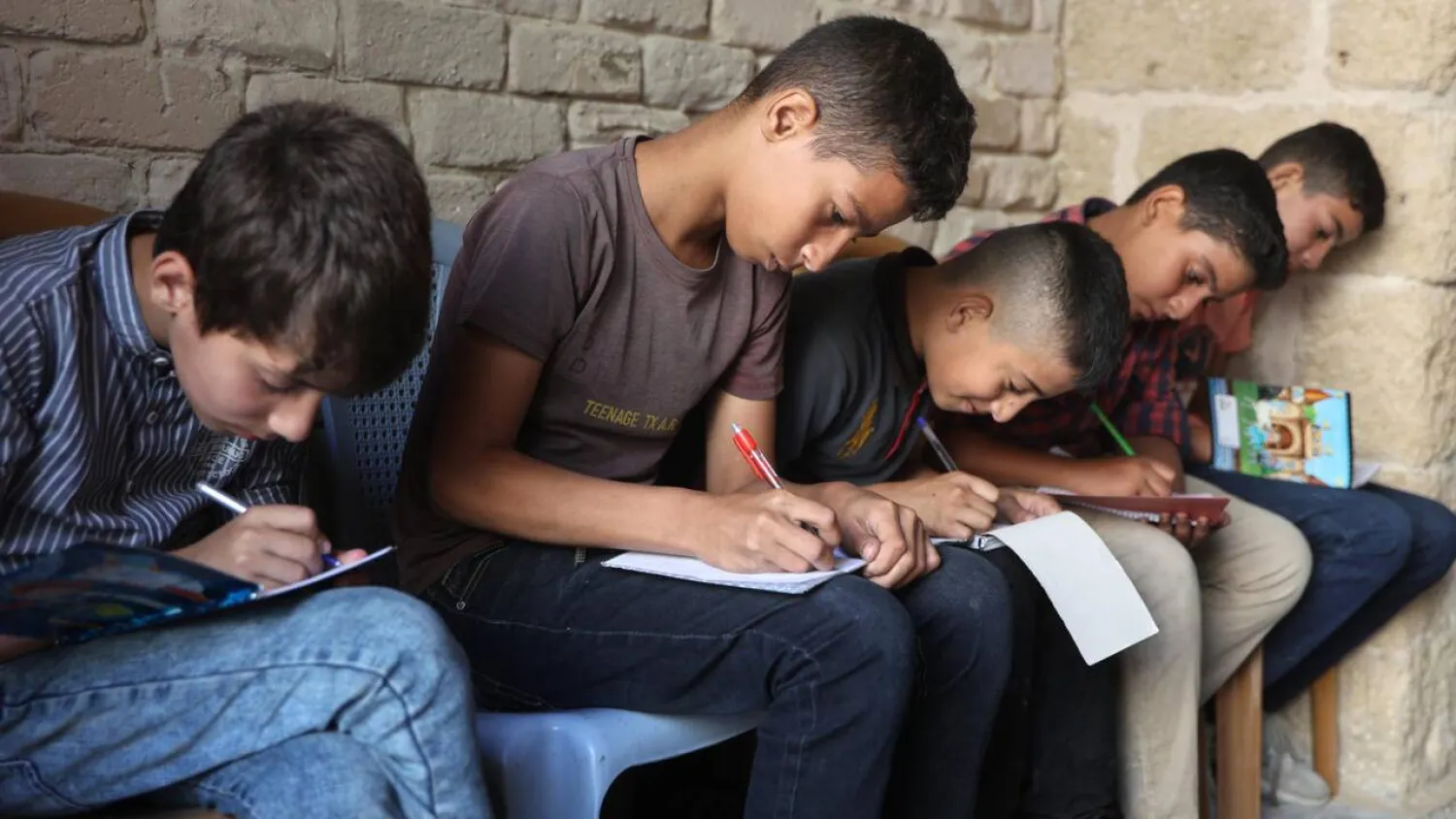 Palestinian children take notes as they attend a class in the historic Al-Kamaliya al-Othmanya school in Gaza City's Old Town, as part of a volunteer initiative organized by displaced teachers, in Gaza City. Omar AL-QATTAA / AFP/File
