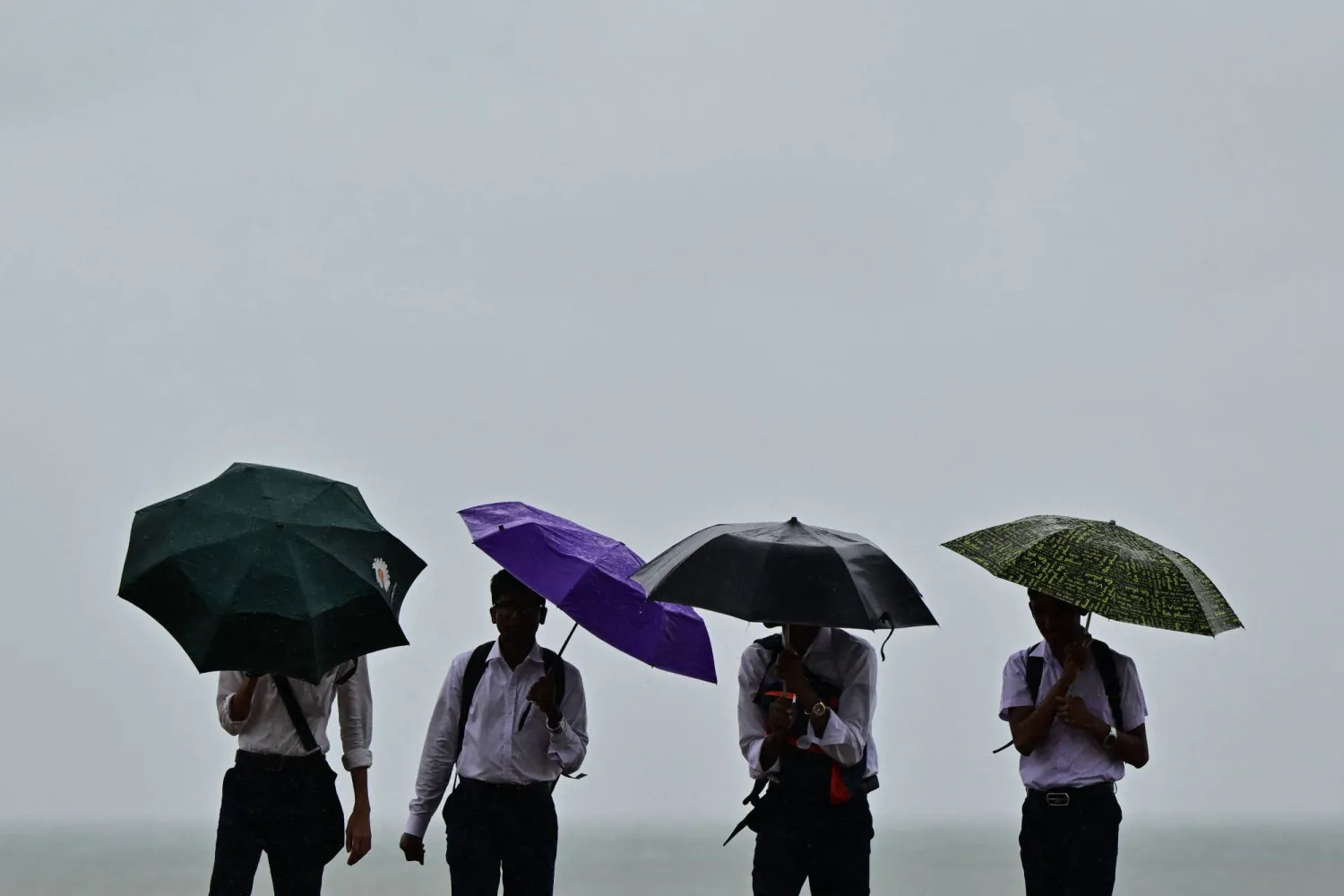 يحمل الناس المظلات وسط هطول الأمطار في كولومبو (أ.ف.ب)