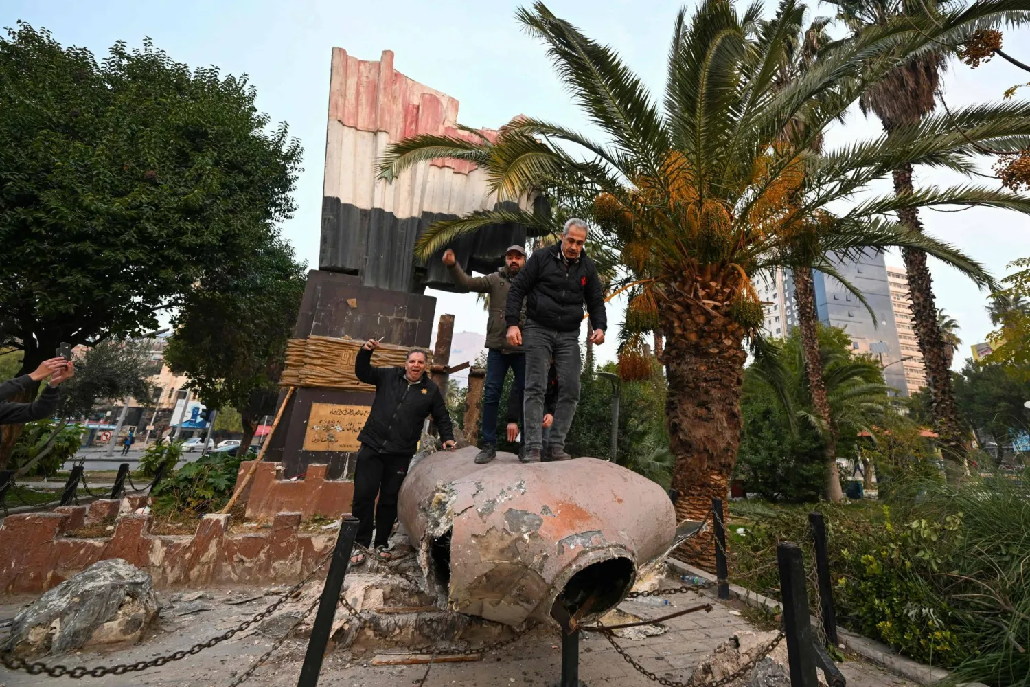 مواطنون يقفون فوق تمثال مقلوب للرئيس السوري الراحل حافظ الأسد في دمشق يوم 8 ديسمبر 2024 (أ.ف.ب)
