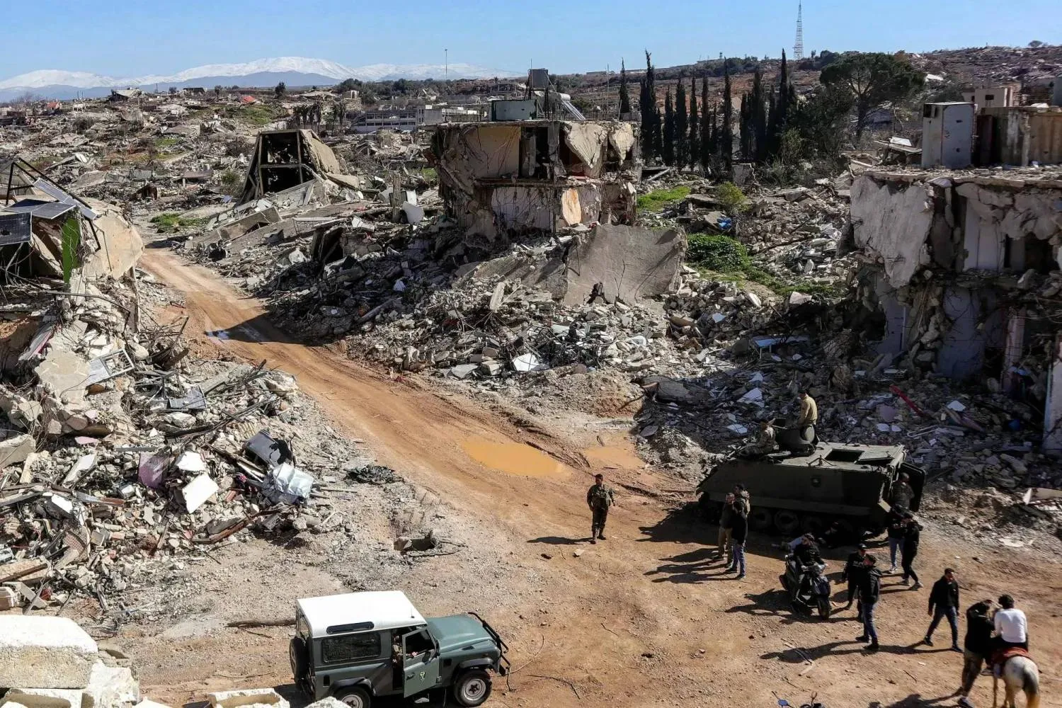 Residents of Kfarkela gather beside Lebanese army vehicles deployed over the ruins of a destroyed building in the southern village (AFP)