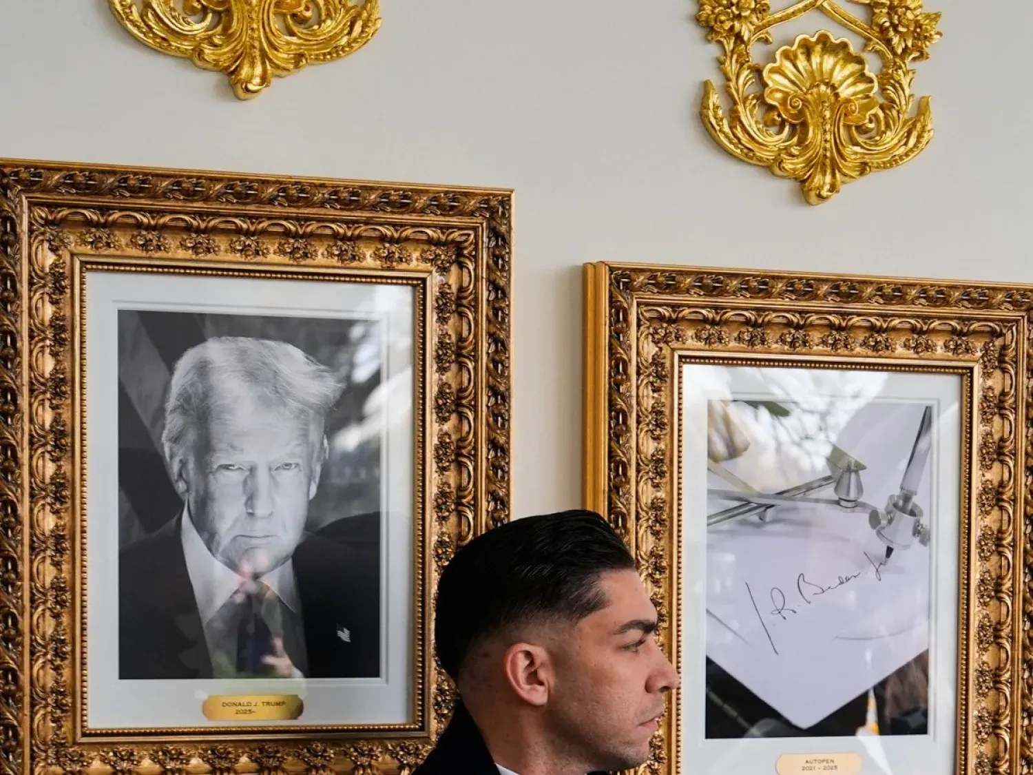 Beyaz Saray koridorlarında Başkan Donald Trump'ın fotoğrafının ve eski Başkan Joe Biden'ın imzasının yer aldığı çerçevelerin önünde duran bir gizli servis ajanı (AP)