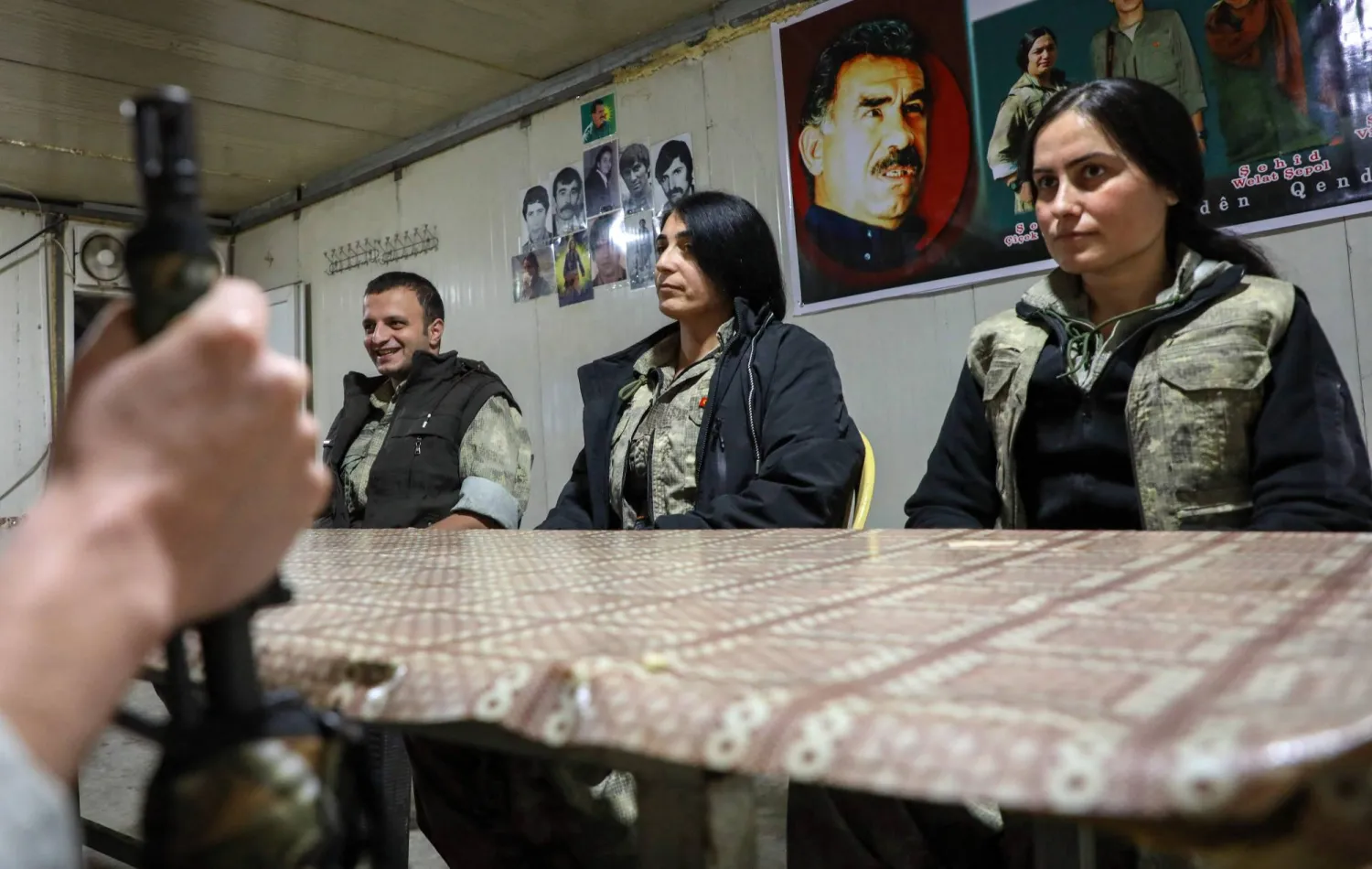 عناصر من حزب «العمال الكردستاني» يجلسون على طاولة وخلفهم صورة للزعيم المسجون عبد الله أوجلان في كهف بجبال قنديل قرب الخدود العراقية التركية أمس (أ.ف.ب)