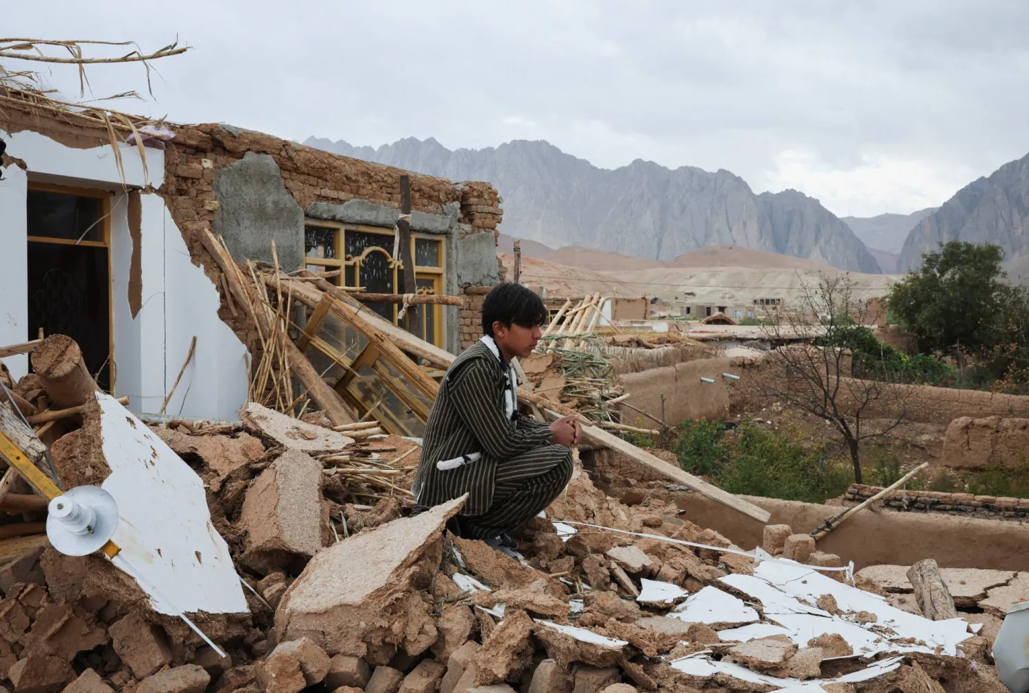 A boy sits next to his damaged house, in the aftermath of an earthquake, in Samangan province, Afghanistan, November 4, 2025. REUTERS/Sayed Hassib