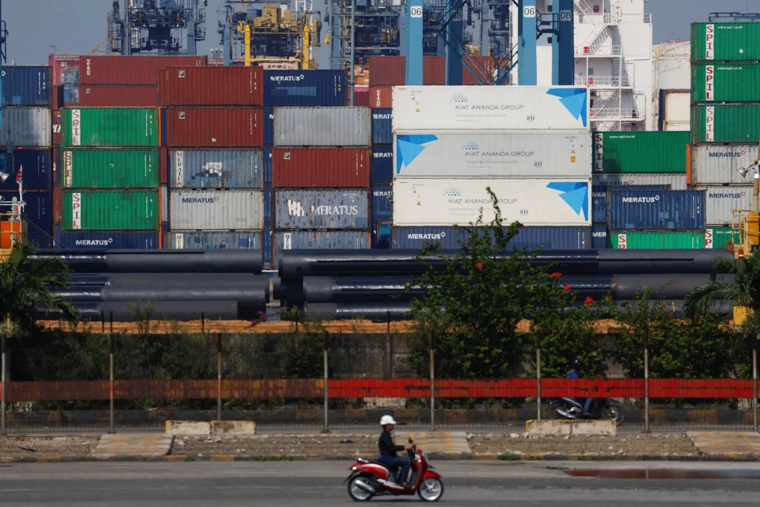 دراجة نارية تمر بجانب أكوام من الحاويات في ميناء تانجونغ بريوك بالعاصمة جاكرتا (رويترز)