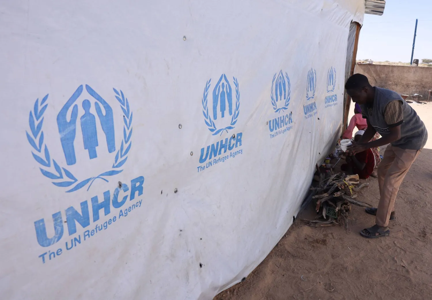 Ibrahim Mohamed Ishaq, 35, a Sudanese refugee father from el-Fasher, stands near firewood after purchasing it for warmth inside the Tine transit camp, after arriving and securing a place in eastern Chad, as he and his family flee ongoing clashes between the paramilitary Rapid Support Forces (RSF) and the Sudanese army, November 22, 2025. (Reuters) 